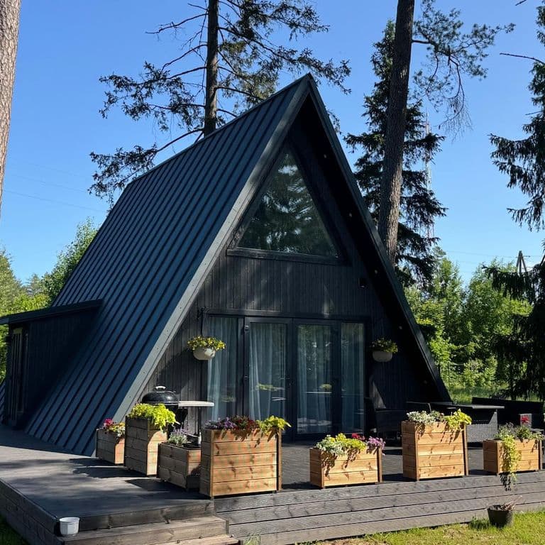 A-veida namiņš starp priedēm ar koka terasi un puķu kastēm